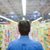 In the supermarket Rear view of man walking along aisle of supermarket